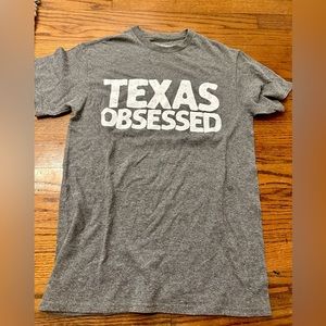 A grey t-shirt with white writing saying “Texas obsessed”.